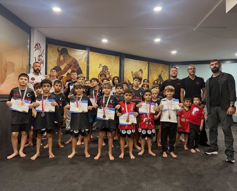 Madalya ve belgeleriyle çocuk sporcular, antrenörleriyle salonda